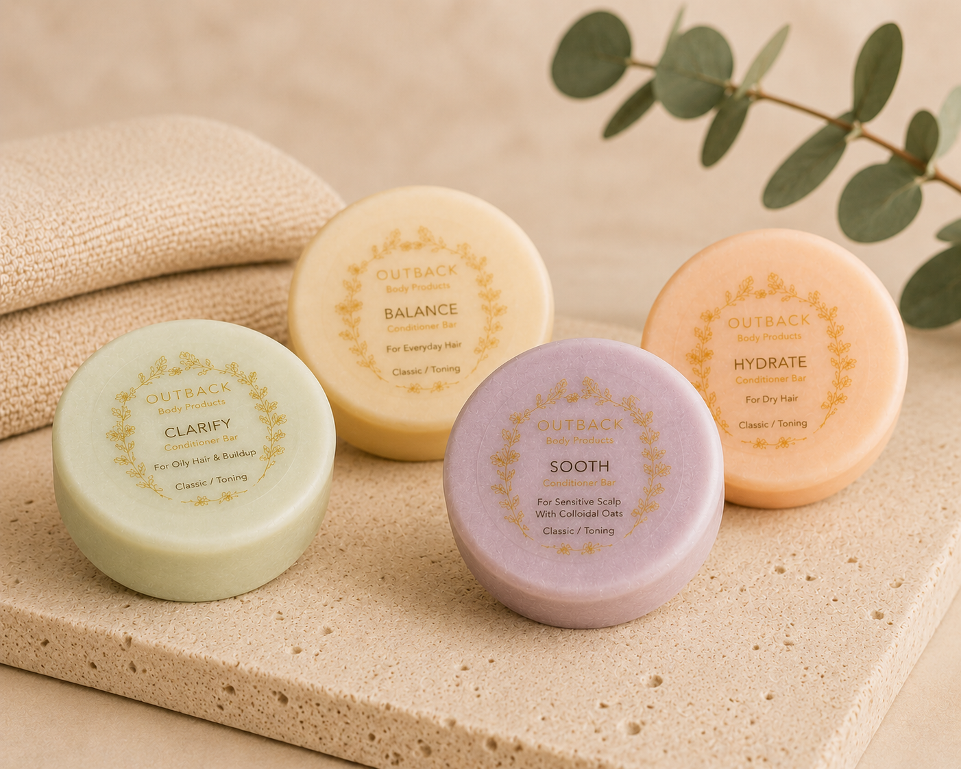 Four round conditioner bars labeled 'Clarify', 'Balance', 'Hydrate', and 'Sooth' on a textured surface with eucalyptus leaves.