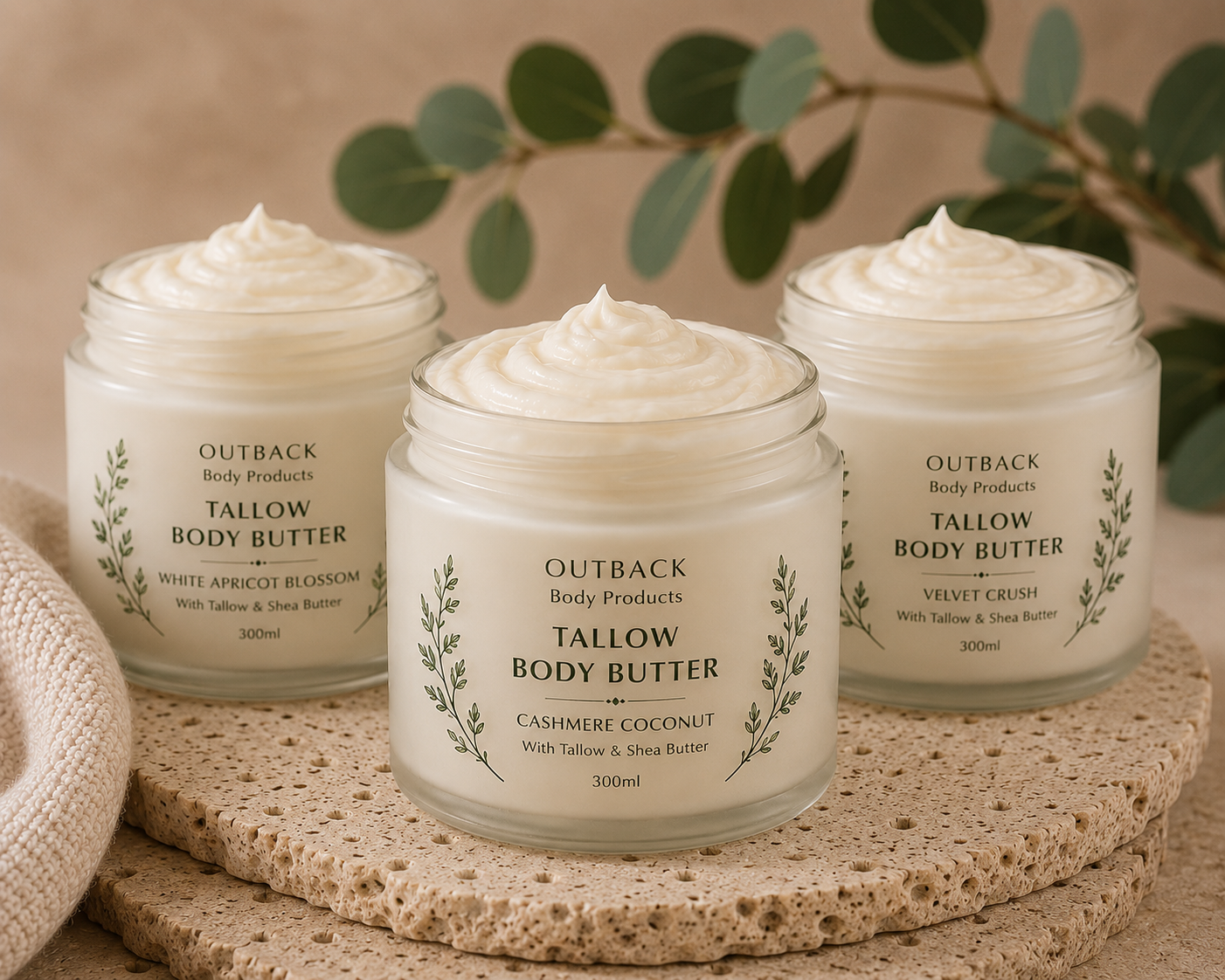 Three jars of Outback Body Products tallow body butter on a textured surface with greenery in the background.