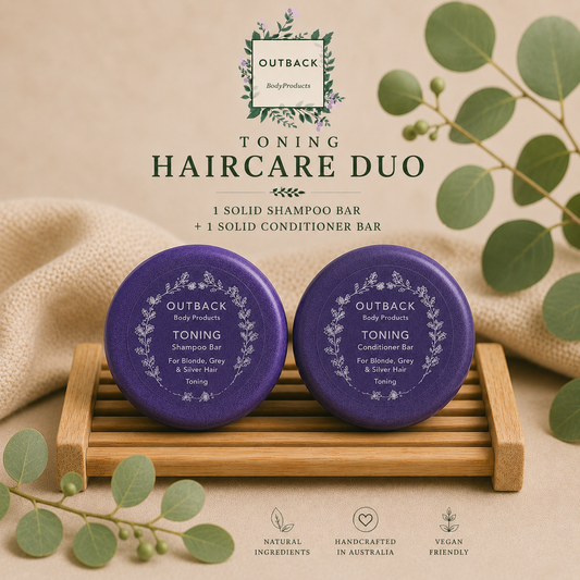 Two purple shampoo and conditioner bars on a wooden stand with green leaves and Outback Body Products branding.