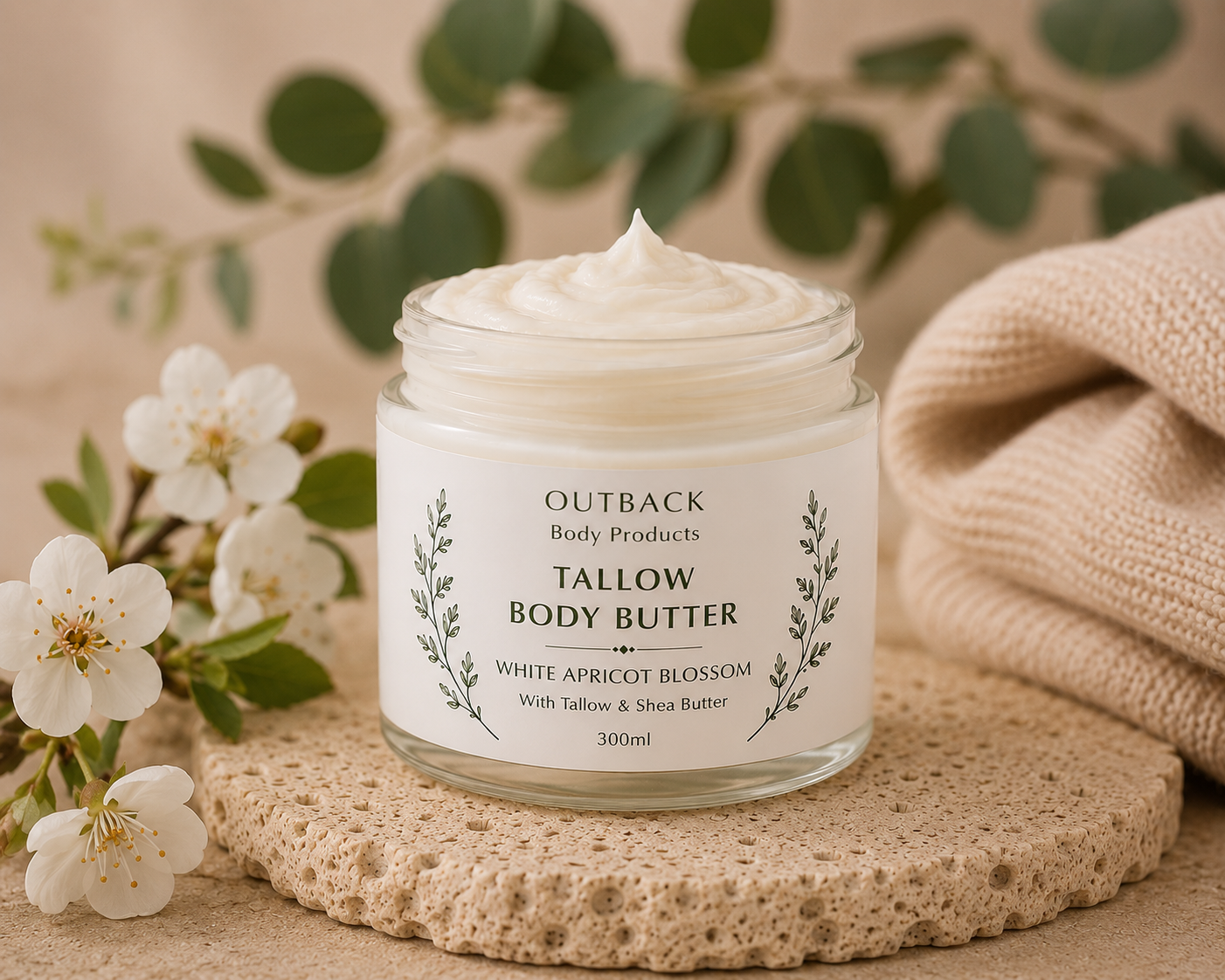 Jar of Outback Tallow Body Butter with flowers and a towel in the background