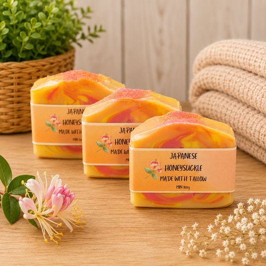 Three bars of soap labeled 'Japanese Honeysuckle' on a wooden surface with flowers and a plant in the background.