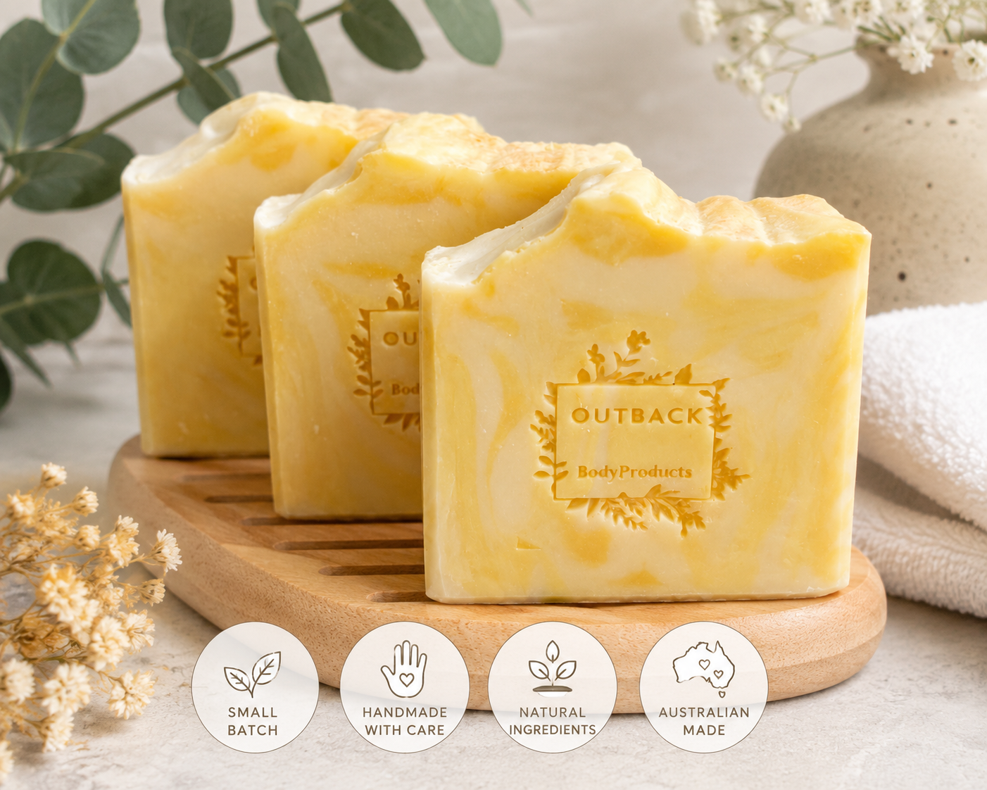 Three bars of yellow soap with 'Outback Body Products' branding on a wooden board, surrounded by decorative elements.