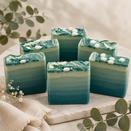 Green and blue layered soap bars on a light surface with greenery around