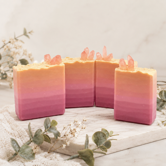 Ombre pink and orange soap bars with crystal-like decorations on a light wooden surface.