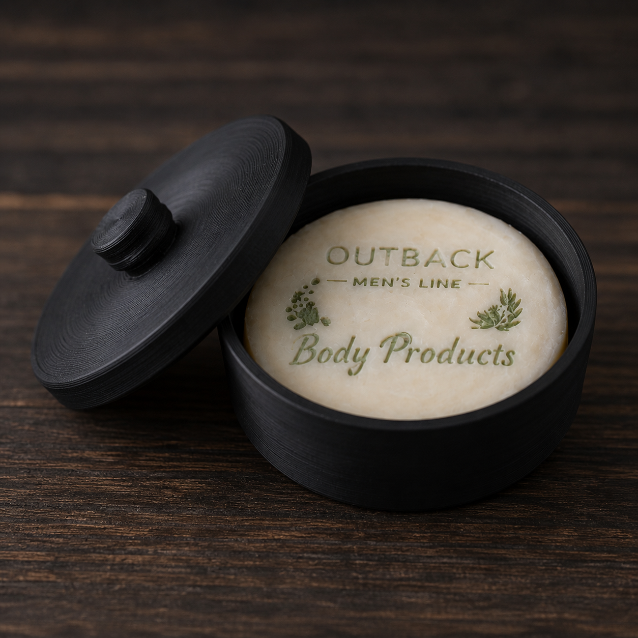Bar of shave soap in a black container with 'Outback Men's Line Body Products' branding on a wooden surface.